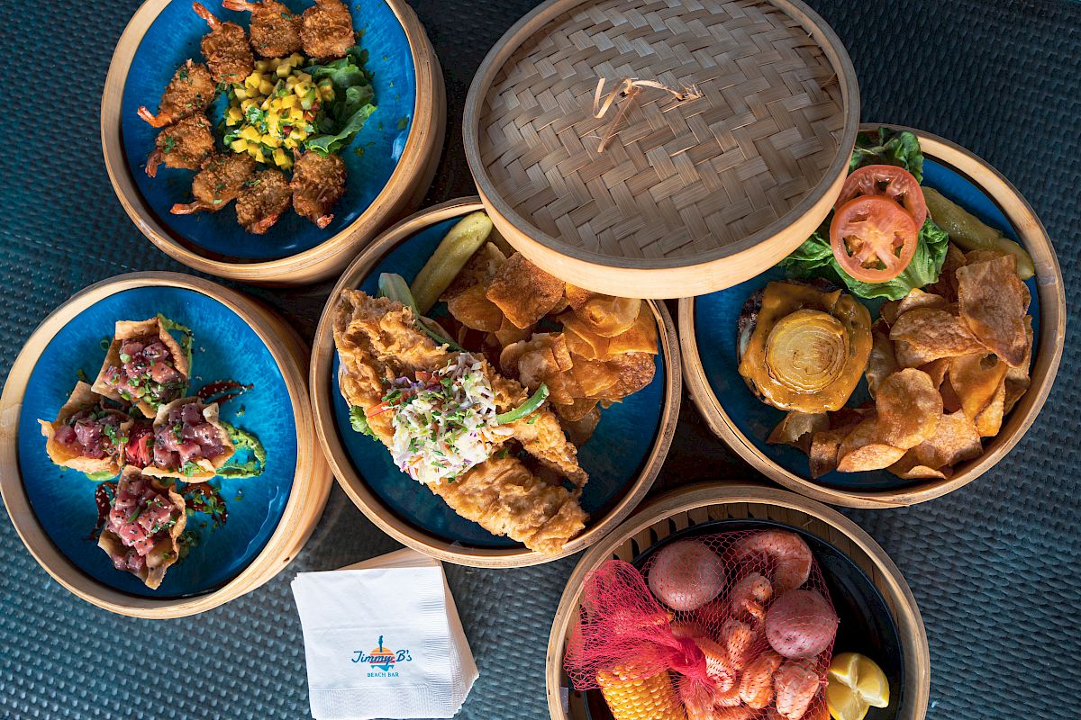 A spread of colorful bowls with fried snacks and toppings, including crispy chips, dips, greens, and a few skewers, arranged in a circular basket set.