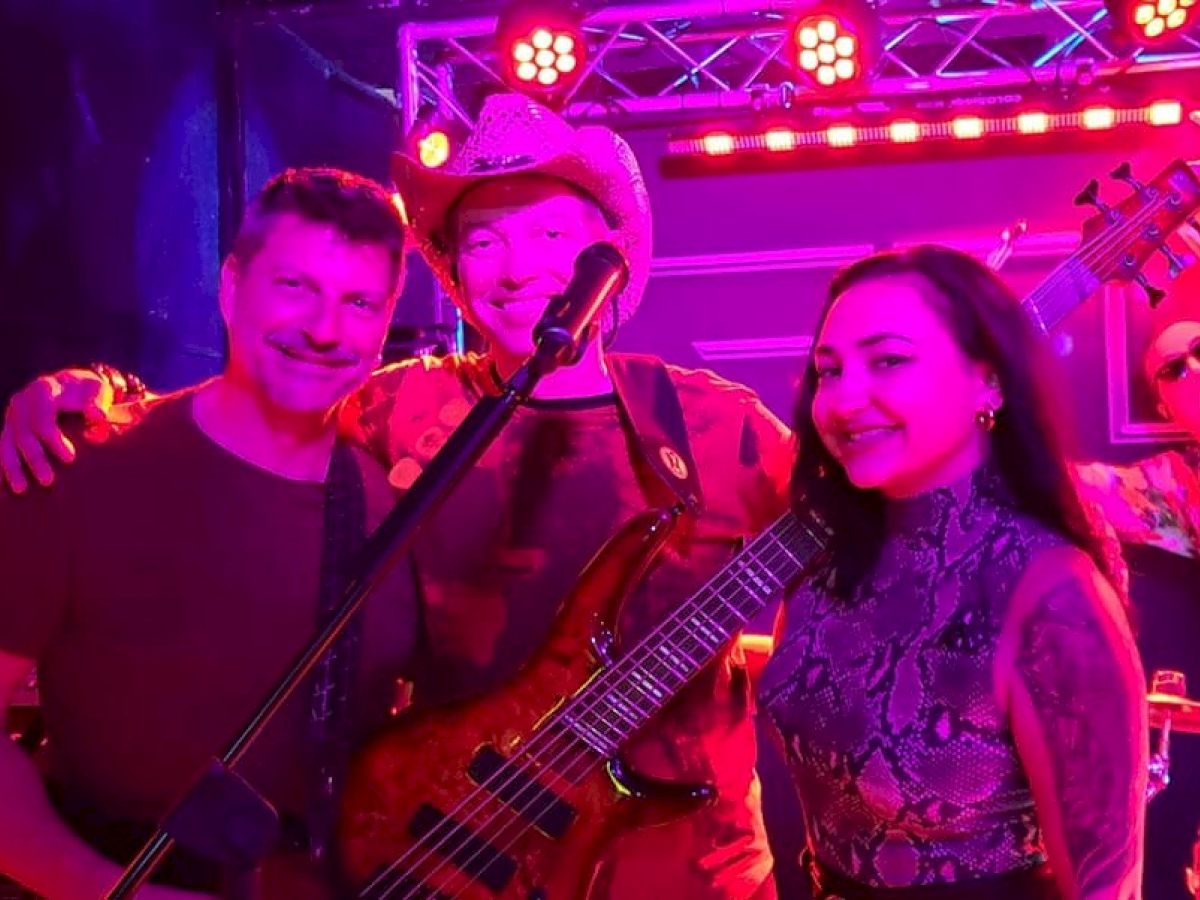 A group of four people at a live music performance, including musicians with instruments and a woman posing with them.