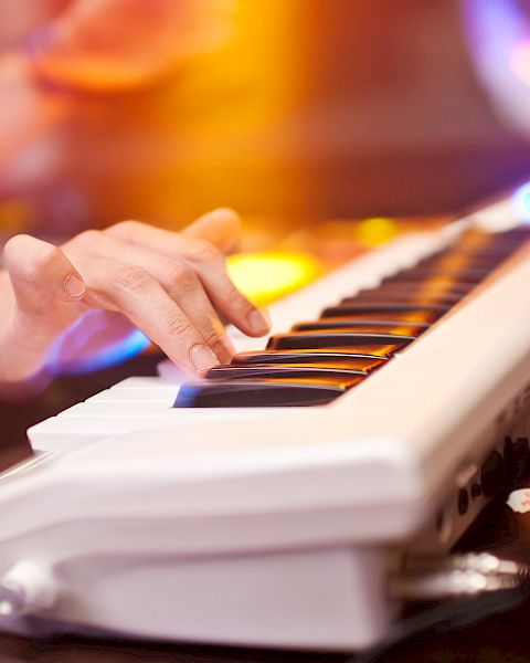 A person is playing an electronic keyboard with colorful lights in the background, creating a dynamic and vibrant atmosphere.