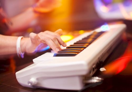 A person is playing an electronic keyboard with colorful lights in the background, creating a dynamic and vibrant atmosphere.