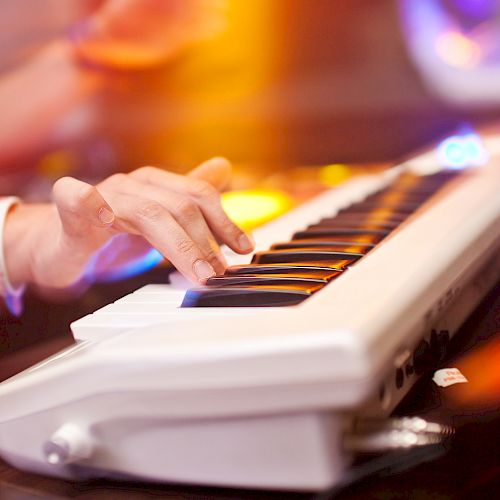 A person is playing an electronic keyboard with colorful lights in the background, creating a dynamic and vibrant atmosphere.