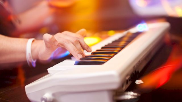 A person is playing an electronic keyboard with colorful lights in the background, creating a dynamic and vibrant atmosphere.