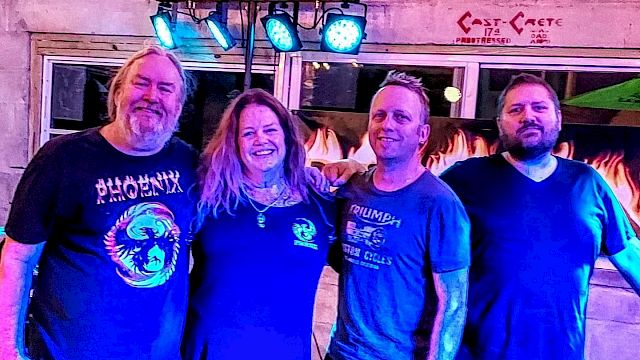 Four people standing together in a well-lit room with colorful lighting, smiling at the camera.