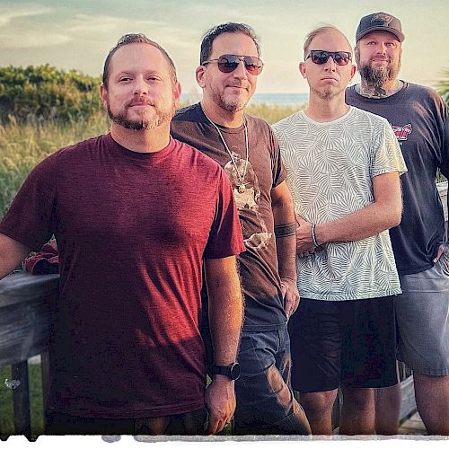 This image features four men standing on a wooden walkway outdoors with text at the top that reads 