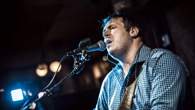 A person is passionately singing or performing into a microphone while playing the guitar in a dimly lit setting.