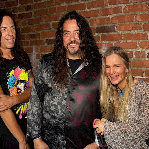 Four people are standing in front of a brick wall, smiling and laughing together.