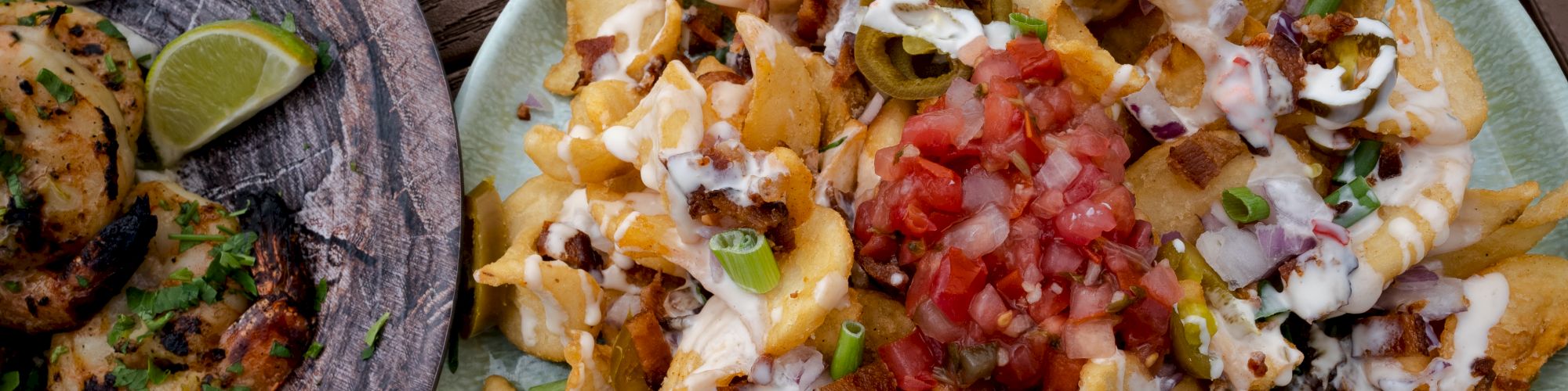 A plate of loaded nachos with toppings like cheese, sour cream, jalapeños, diced tomatoes, and green onions next to grilled chicken and a lime wedge.