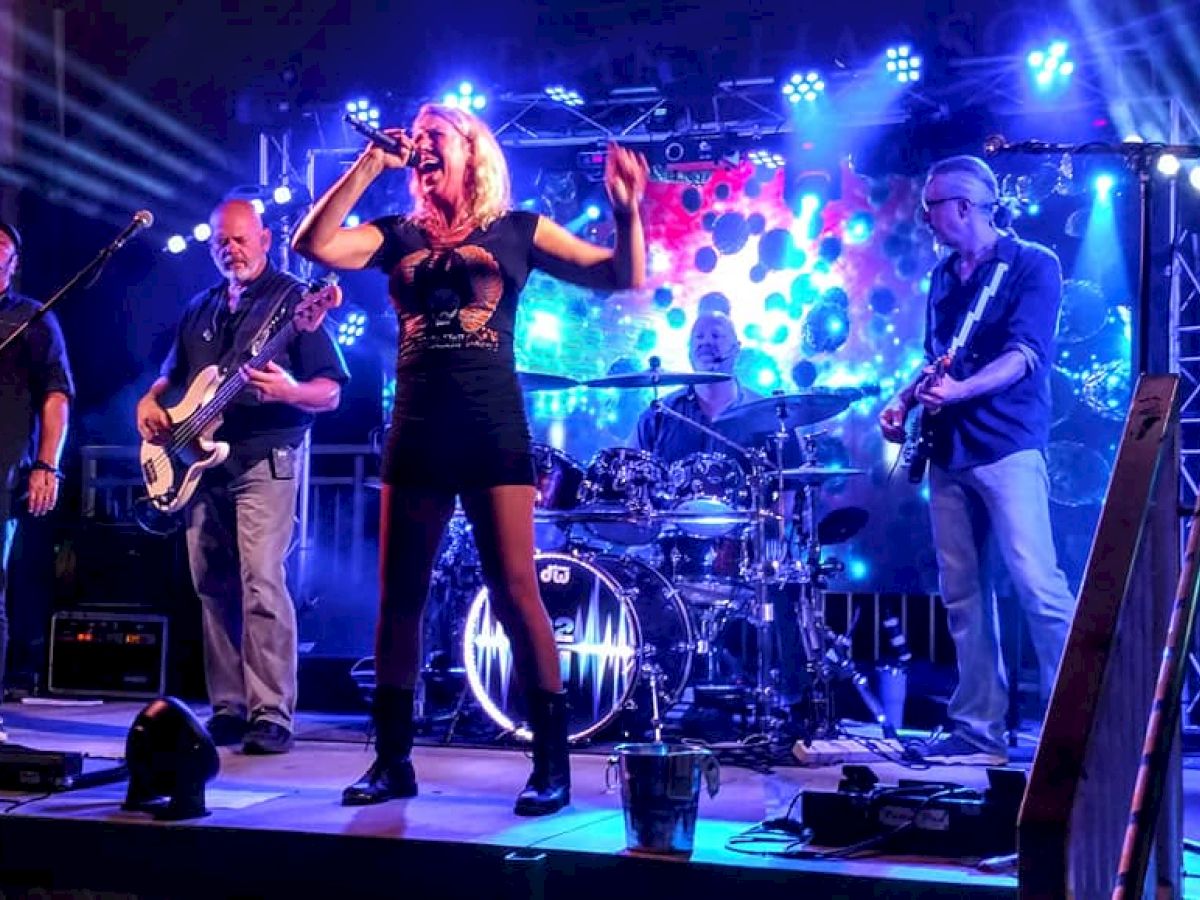 A band performs on stage with various instruments and a vibrant lighting setup in the background. The vocalist is center stage.