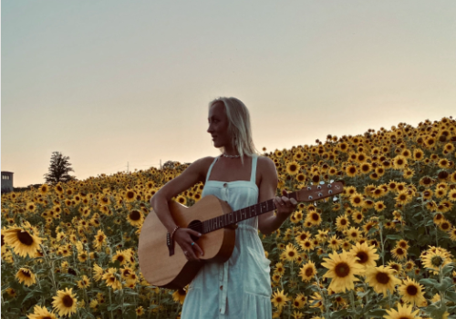 A young woman with a guitar in a field of sunflowers.