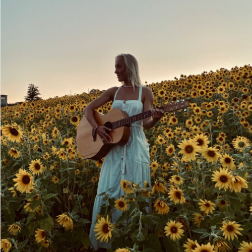 A young woman with a guitar in a field of sunflowers.