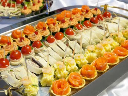 A tray of assorted canapés with various toppings including salmon, cheese, tomatoes, and other garnishes arranged neatly for serving.