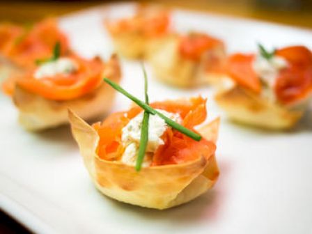 The image shows a plate of bite-sized appetizers, possibly with smoked salmon, cream cheese, and herbs served in crispy pastry cups.