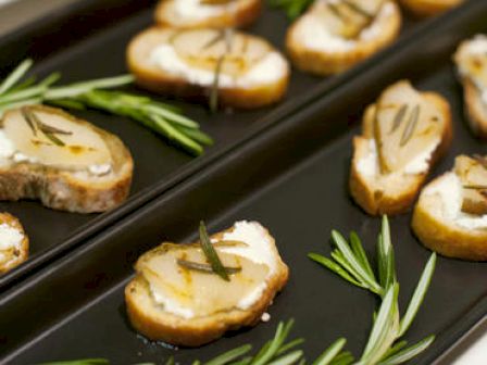 Sliced bread topped with cheese and garnished with herbs is displayed on two black trays, with rosemary sprigs for decoration ending the sentence.