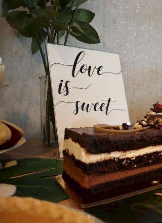 A dessert table with a chocolate layer cake, roses, and a sign that reads 