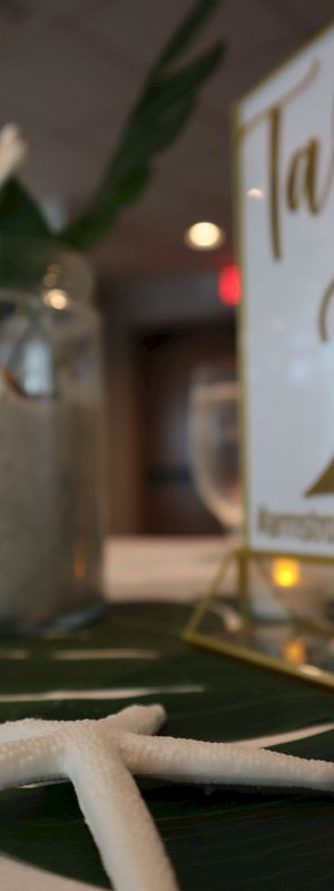 A table centerpiece with a starfish, candle, floral arrangement in a jar, and a sign indicating 