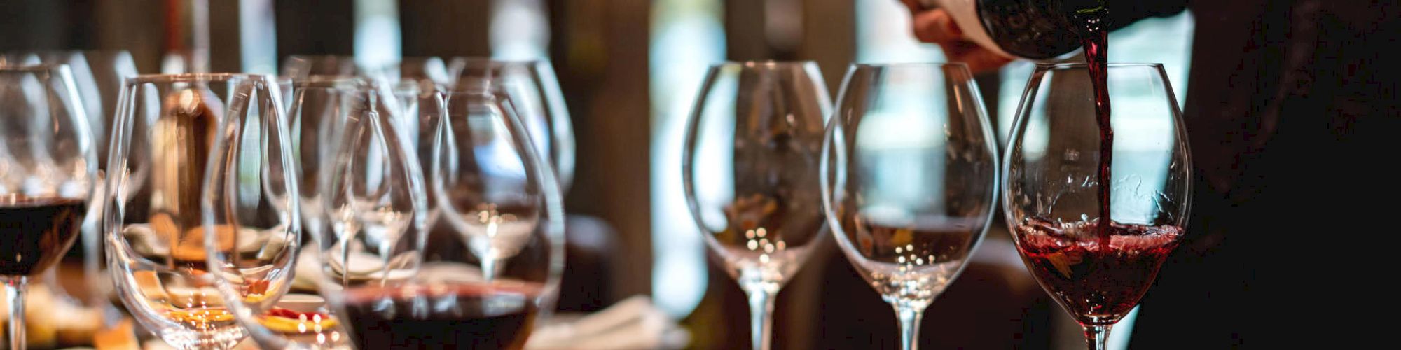 A person pours red wine into glasses on a table set with various cheeses, meats, and bread, creating an inviting spread for a gathering.