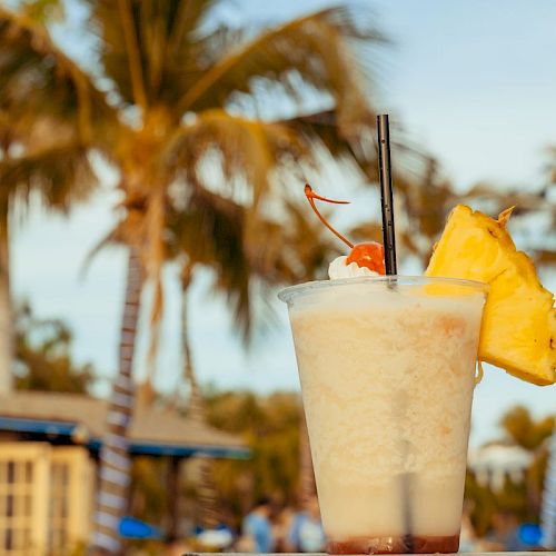 A tropical cocktail with a cherry, umbrella, and pineapple slice is set against a background of palm trees and a beachside bar.