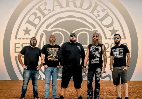 Five men with beards stand outdoors in front of a sign that says 