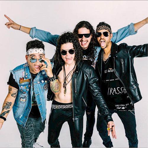 Four men are posing excitedly in rock-style outfits, wearing sunglasses and various accessories, against a plain white background.