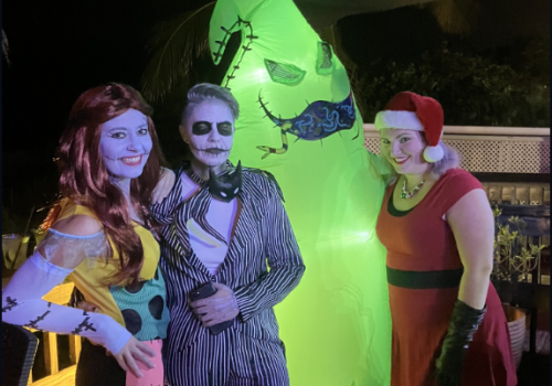 Four people are in costumes, three in character outfits and one in a large green inflatable suit, standing together in a dimly lit area.