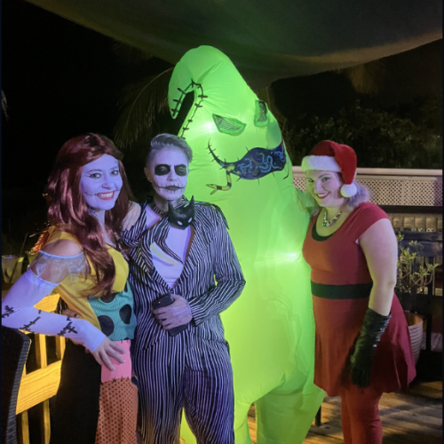 Four people are in costumes, three in character outfits and one in a large green inflatable suit, standing together in a dimly lit area.