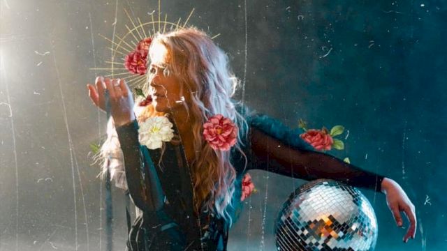 A person sits on the ground holding flowers, with a disco ball nearby. The background is dark and ethereal, with a mystical and artistic atmosphere.