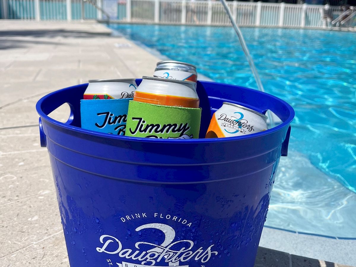 A blue bucket filled with cans is placed beside a pool with palm trees in the background, under a clear sky.