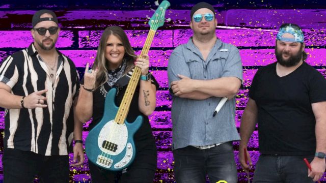 A group of four people posing in front of a purple brick wall; one holds a blue guitar, and they all appear dressed in casual attire.