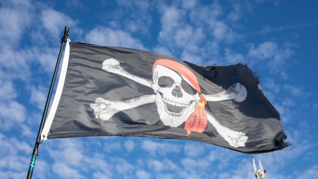 Pirate flag with a skull and crossed bones fluttering against a bright blue sky.