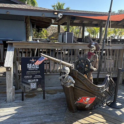 Skeleton pirates man a wooden ship in a dockside setting; signboard and cheerful backdrop under a sunny sky.