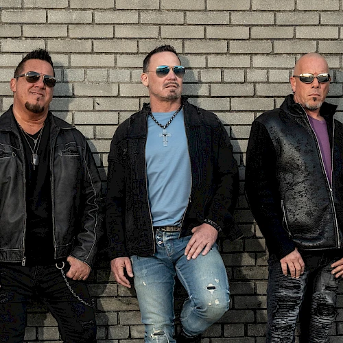 A group of five men wearing black leather jackets, posing against a brick wall, looking tough and stylish with sunglasses, biker vibes.